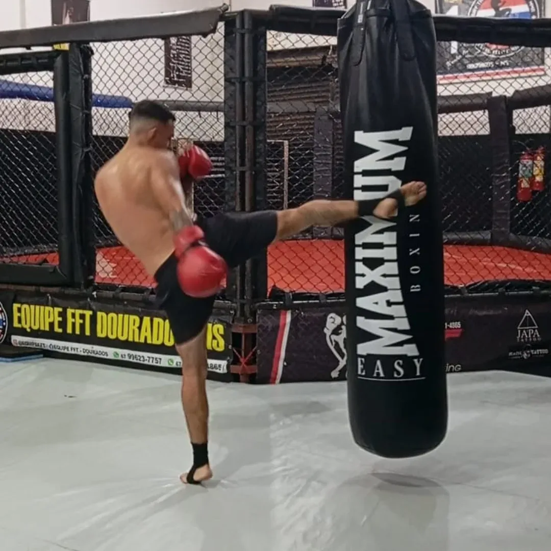 Atleta da Equipe FFT aplicando chute alto no saco de pancadas durante treino de Muay Thai em Dourados