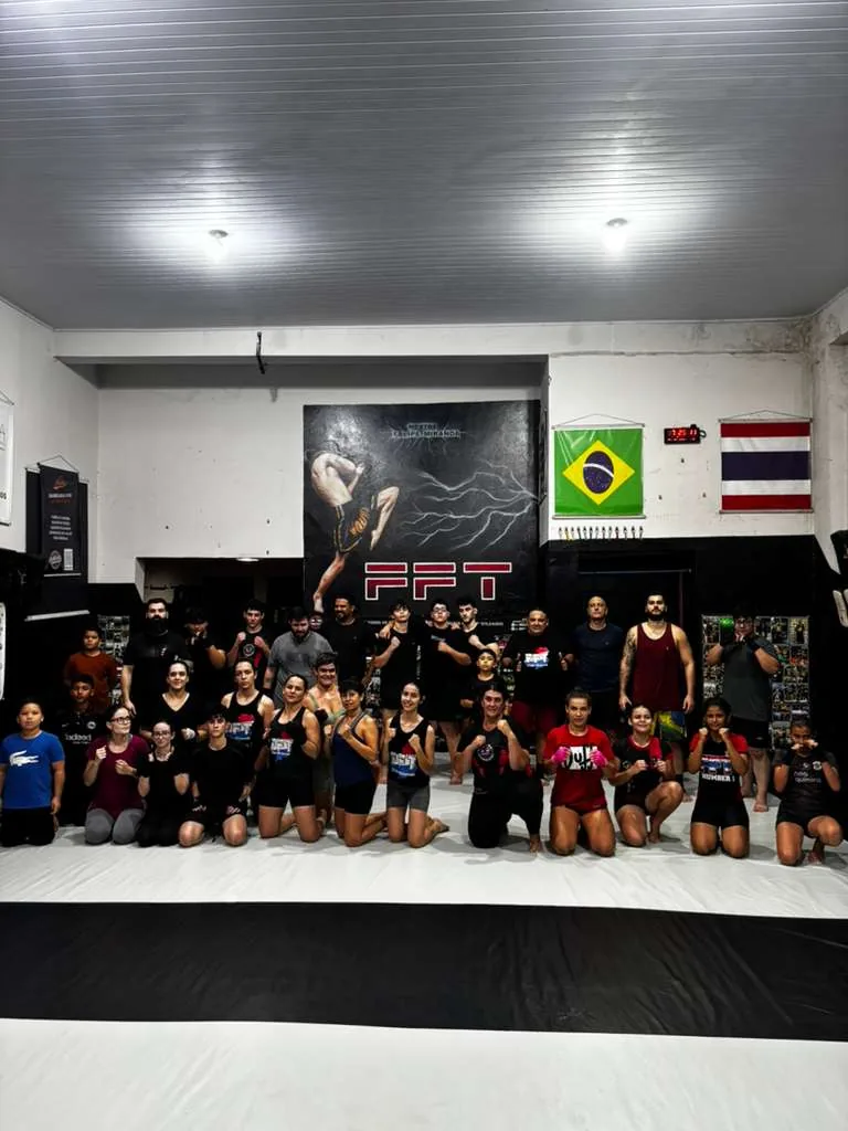 Equipe FFT reunida no tatame da academia em Dourados-MS, sob a bandeira da equipe e as bandeiras do Brasil e da Tailândia