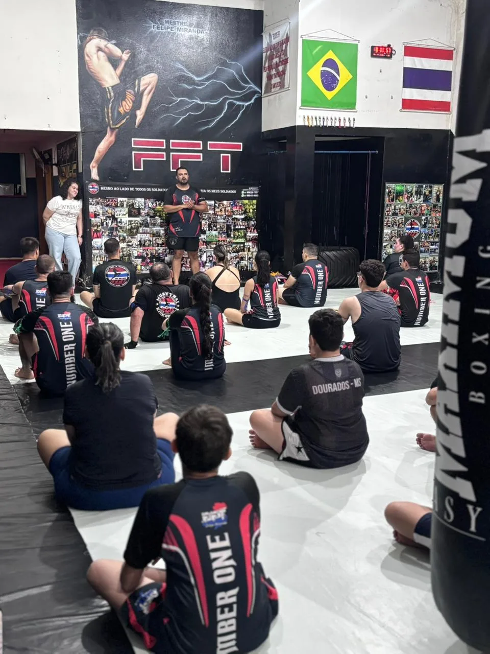 Turma de iniciantes sentada no tatame da Equipe FFT ouvindo a explicação do professor antes do treino